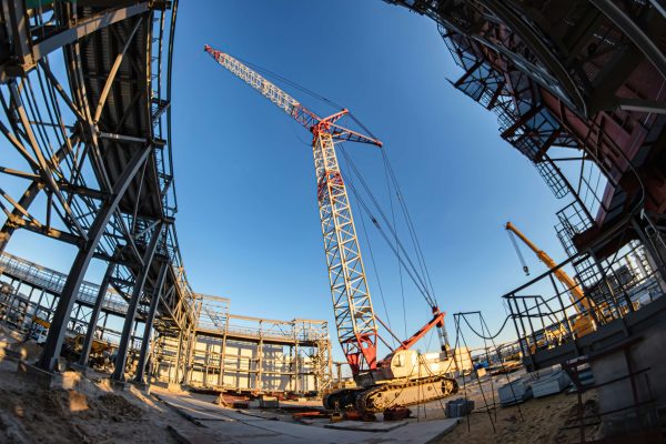 A crane stands prominently in the center of a busy construction site, surrounded by building materials and equipment.