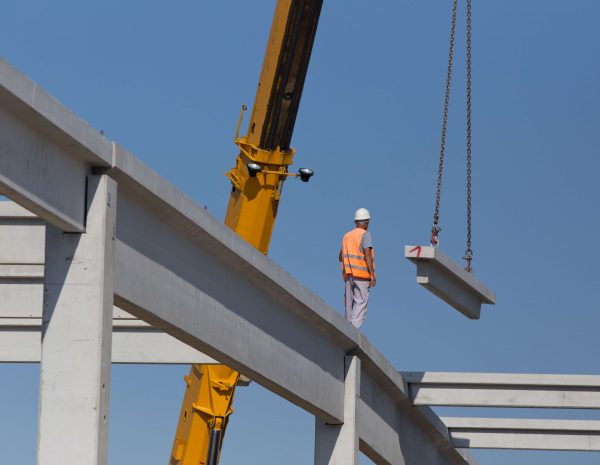 A man stands on a construction site, observing a crane in the background, surrounded by building materials and equipment.