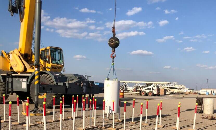 A crane lifts a large object above a field, showcasing construction or heavy lifting in progress.