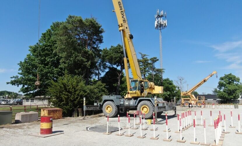  A crane lifts a large object on a dirt lot, showcasing construction activity in progress.